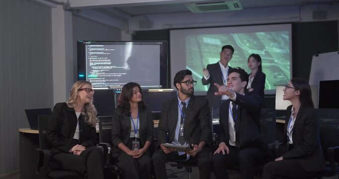 Diverse business team gathers for roundtable presentation in tech office, with a presenter leading discussion as colleagues review documents and screens. Collaboration, training, strategic planning
