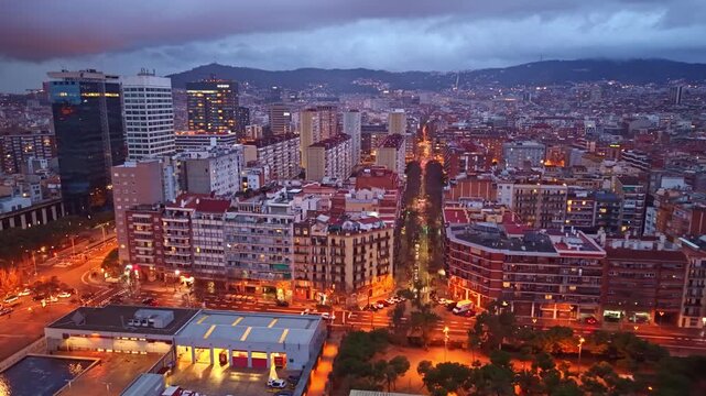 Slow aerial pan at night over La Nova Esquerra de l&rsquo;Eixample in Barcelona, revealing Carrer de Tarragona as a luminous vertical axis, and the city stretching toward the Collserola hills.