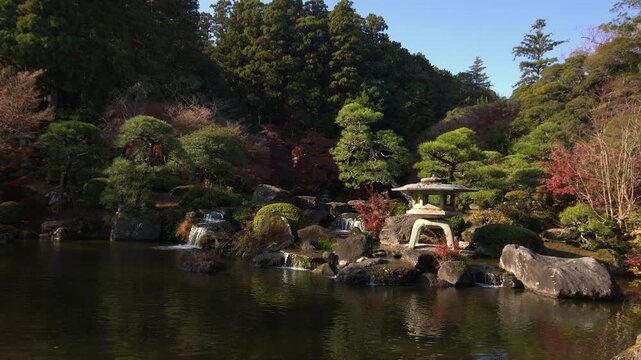 Water falls into Ryuchi pond by old stone lantern in Naritasan Park