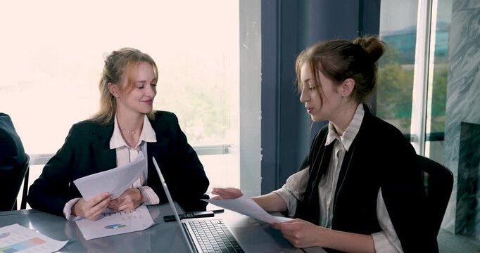 Multiracial businesswomen reviewing colorful financial chart and report together during team meeting while discussing planning strategy for corporate success in bright modern office