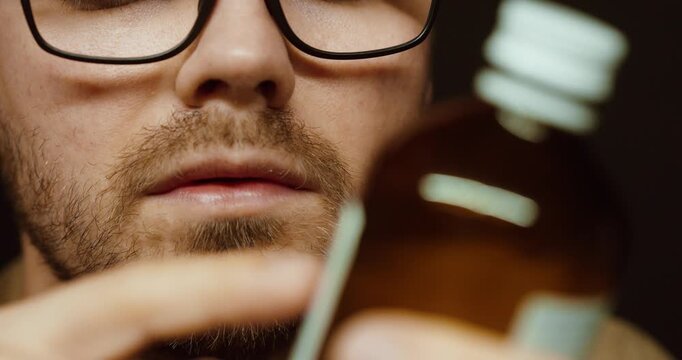 Close-up of a man with glasses carefully reading the label on a medicine bottle. Concept of healthcare, medication safety, dosage checking, and medical awareness.