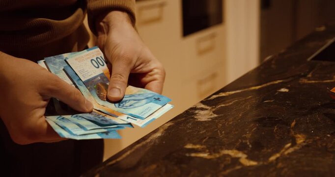 Close-up of hands counting Swiss franc banknotes on a kitchen counter. Concept of personal finance, budgeting, cash management, household expenses, and money handling at home.