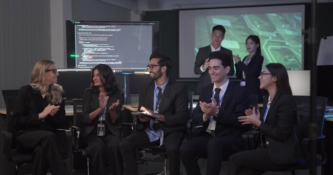 Diverse business team gathers for roundtable presentation in tech office, with a presenter leading discussion as colleagues review documents and screens. Collaboration, training, strategic planning
