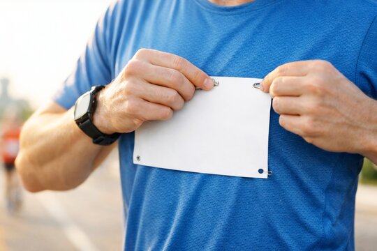 Runner attaching blank bib number to blue t-shirt with safety pins, close-up view