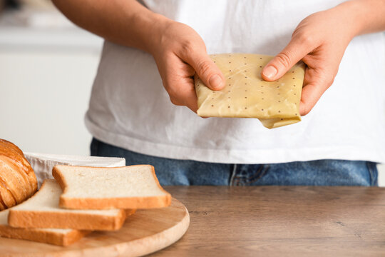 Young woman with fresh bread slices wrapped in beeswax paper on table at home, closeup