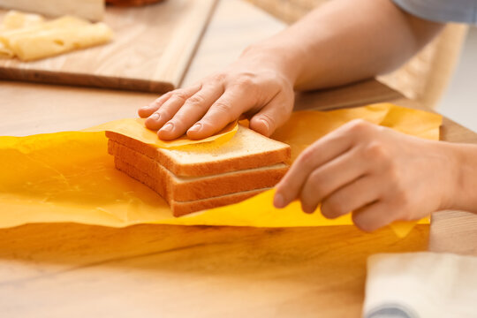 Young woman wrapping fresh bread slices in beeswax paper on table at home, closeup