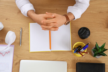 Young businessman with stationery, headphones and notebook at table in office, top view