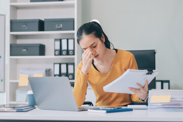 Young professional woman suffering from headache while analyzing financial charts and graphs on computer, experiencing work related stress in modern office