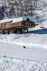 Snowboarder riding on slope past a snow-covered ski lift station at Togari Onsen