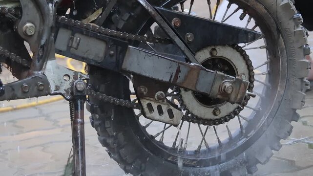 Satisfying power wash of dirty, muddy motorcycle. gritty, close look at rear wheel, chain, and disc brake during deep cleaning maintenance routine