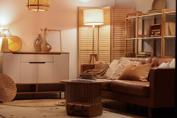 Interior of living room with bookshelf, sofa and glowing lamps in evening