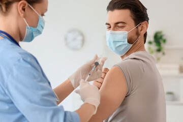 Young man with medical mask receiving vaccine from doctor in clinic