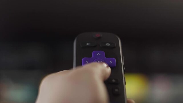 Person navigating a smart tv menu with a roku remote control for streaming media and watching online content