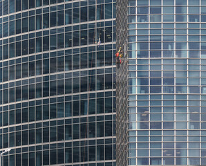 Obraz premium Window washers cleaning the glass facade of a modern skyscraper with reflective surfaces and geometric patterns in an urban setting