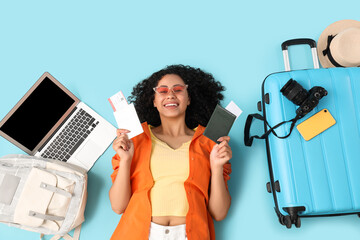 Young female African-American tourist with passport, tickets, laptop and travelling accessories...