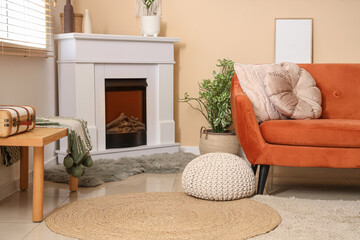 Naklejka premium Fireplace, sofa and pouf near beige wall in interior of room, closeup