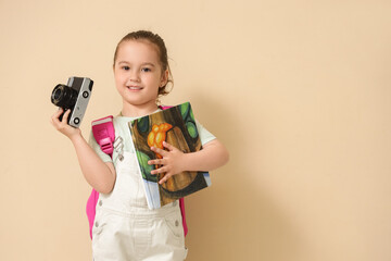 Naklejka premium Cute little girl with adventure book and photo camera on beige background