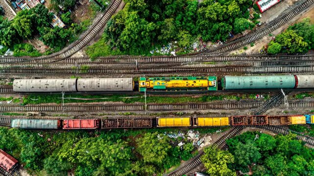 Overhead aerial view of railway tracks and trains amongst green foliage, urban sprawl visible