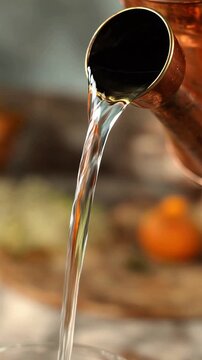 Clear water pouring from a vintage copper kettle into a glass, close-up shot