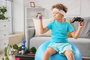 Thoughtful little boy on fitball choosing between dumbbell and game pad at home © Pixel-Shot