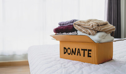Cardboard box filled with used clothing with the word "Donate." Idea of ​​donating clothes to charity.