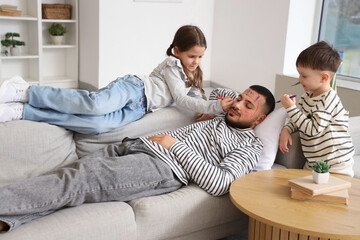 Little children painting their father's face while he sleeping at home. April fool's day prank