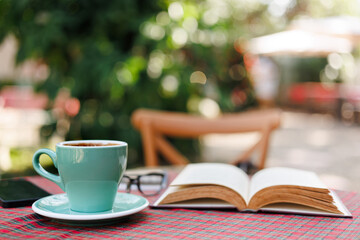 close up shot, green ceramic mug with open book on table with red tablecloth, outdoor view, blurred backgroung and bokeh, relax on holiday