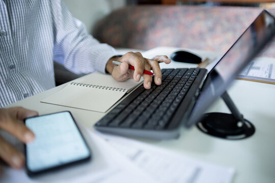 asian businessman work at home typing on computer keybord working online with tablet, mobile phone and note book on desk