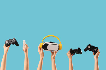 Naklejka premium Female hands with game pads, VR glasses and headphones on blue background