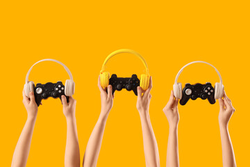 Female hands with game pads and headphones on yellow background © Pixel-Shot