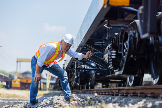 Railway engineer checking the undercarriage and wheel system of a freight train at a rail yard. Concept of rail safety inspection, maintenance engineering, logistics operations, and infrastructure rel