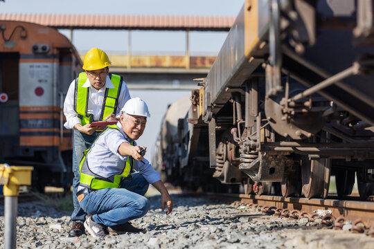 Railway engineer checking the undercarriage and wheel system of a freight train at a rail yard. Concept of rail safety inspection, maintenance engineering, logistics operations, and infrastructure rel