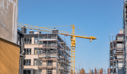 Apartment block under construction with a large yellow crane. Building site with scaffolding for urban development and real estate. © Anton Dios