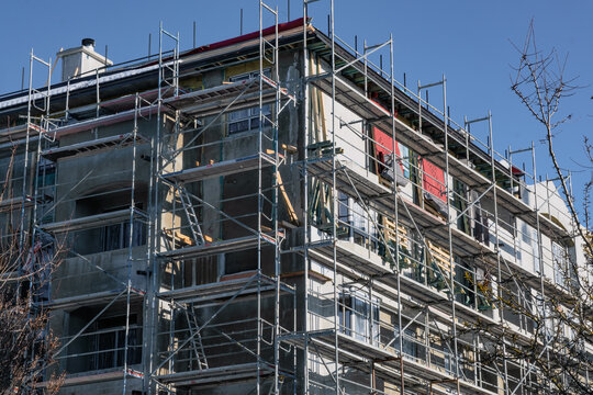 Facade of a building under renovation with scaffold surrounding it, showing windows and construction site activity