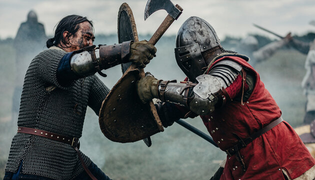 Dramatic close-up of two medieval warriors in armor fighting with an axe and shield during a historical battle reenactment.