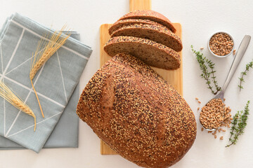 Wooden board with sliced loaf of bread, wheat spikelets, grains and thyme on white background