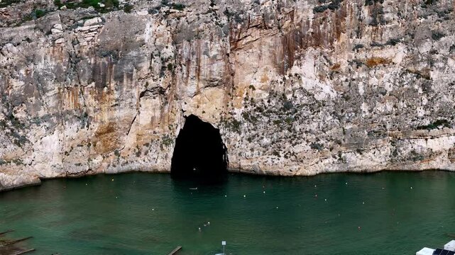 Spectacular low angle view inside the famous Inland Sea tunnel at Dwejra Gozo during a sunny summer day featuring a traditional luzzu boat navigating the turquoise water through limestone sea caves