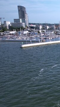 A scenic wide shot of the Gdynia Marina in Poland featuring the iconic Sea Towers skyscraper, numerous luxury yachts, and the Baltic Sea harbor.