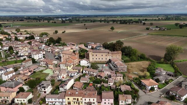 Drone push-in over the village of Calendasco in the Piacenza province, featuring the medieval Castello di Calendasco, the Church of Santa Maria Assunta, and the expansive rural Po Valley farmland