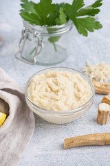 Horseradish sauce in glass bowl with lemon and horseradish roots on white background