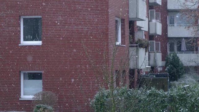 Red brick architectural apartment blocks in the background, snow falling in the foreground in slow motion.