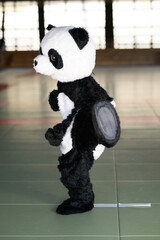 道場で鋭い上段蹴りを繰り出すパンダの着ぐるみ　ユニークな空手の武道イメージ