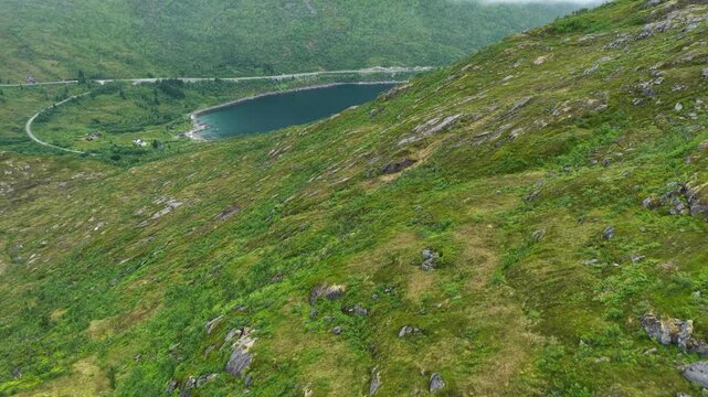 Aerial, forward drone flight above Norwegian mountains, trail to Barden mountain. Grassy mountain slope with rocks. Small lake and hiking parth in distance. Senja island in Norway. Beautiful landscape