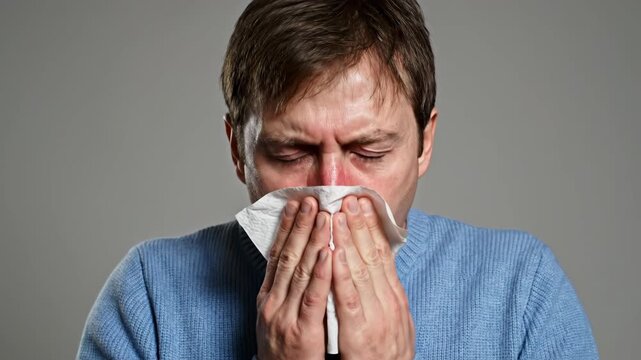 Close-up of a man blowing his nose with a tissue. Male suffering from a cold or flu symptoms. Illness and healthcare concept