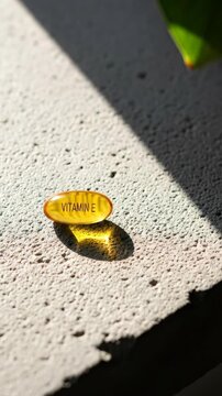 Vitamin E yellow caplet on white concrete with changing light and plant shadow, concept of health supplement