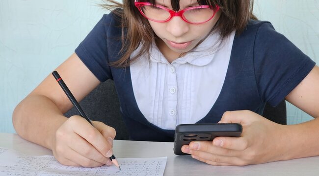 Serious kid doing classwork using smartphone in class and mobile education