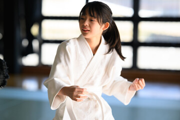 道場で鋭い眼差しで後ろを振り返り蹴りを放つ空手着の女の子　護身術と防犯のイメージ