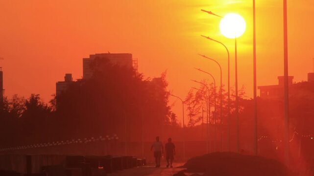 4k cinematic sunset b-roll of silhouette people walking along coast on sidewalk while sun is going down behind buildings Phan Thiet, Vietnam
