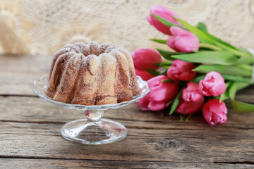 Traditional Easter cake on wooden table. Beautiful bouquet of pink tulips in the background.