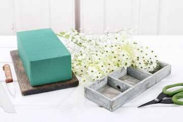 Florist at work: woman shows how to make Easter floral table decoration with arabian star flowers and gypsophila paniculata twigs in simple wooden box. Step by step, tutorial.